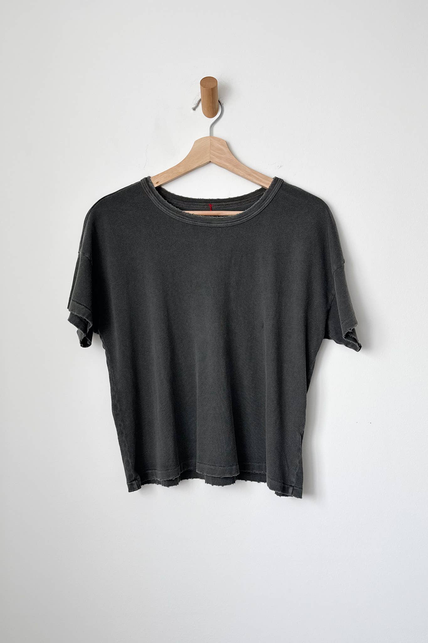 A washed black t-shirt hanging on a wooden hanger against a white wall.