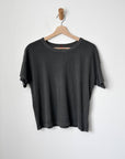 A washed black t-shirt hanging on a wooden hanger against a white wall.