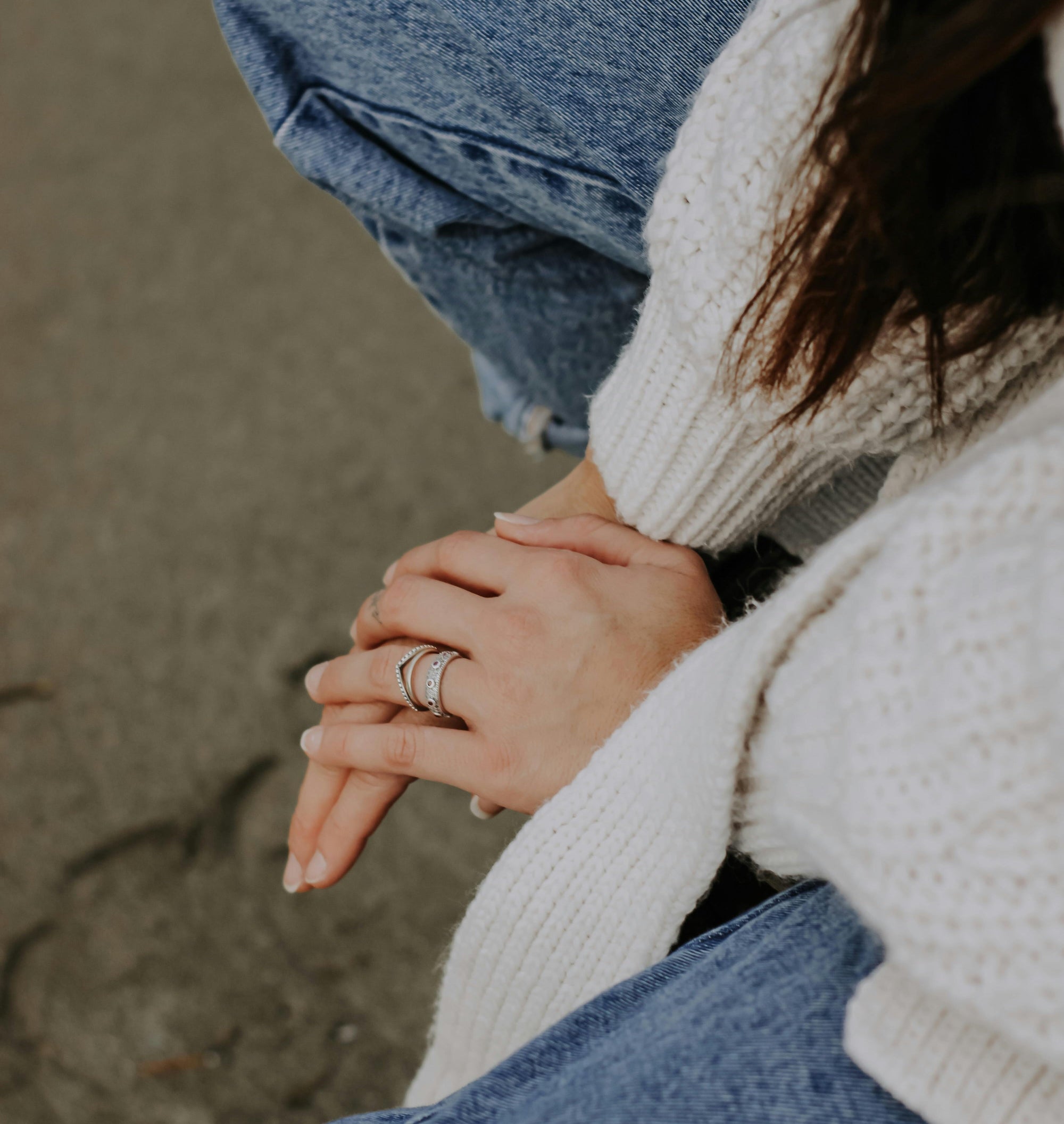 woman's hands wearing rings, with jeans and a cream knit sweater