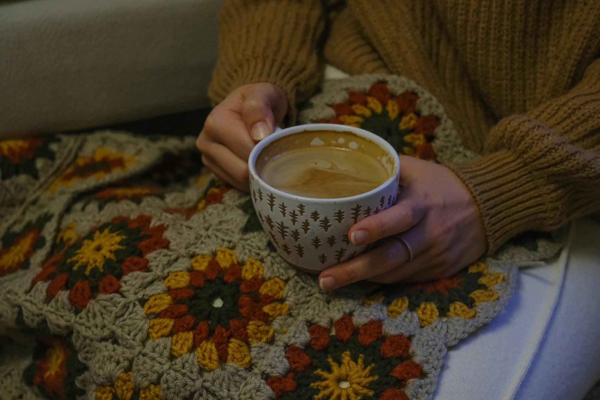 hands holding a ceramic mug with tea over an afghan blanket